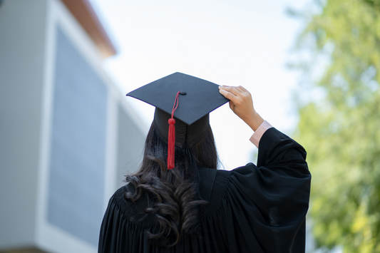 Back of woman wearing graduation outfit holding graduation cap