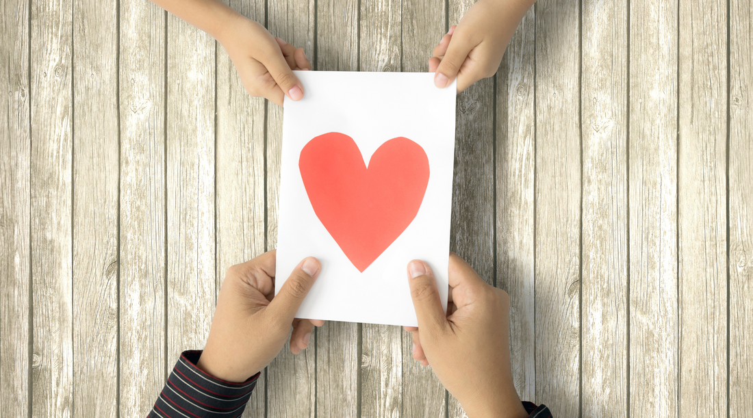 Two sets of hands holding a white card with a read heart on it